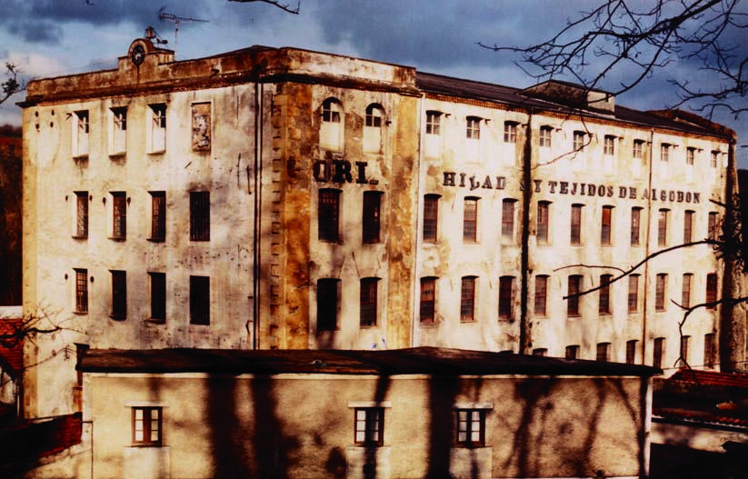 Fotografía en color del edificio de hilatura de Oria, con el reloj y el rótulo pintado en la fachada.